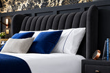 A modern bed with a tall, channel-tufted upholstered headboard in dark charcoal gray velvet, styled with white and blue pillows and bedding.