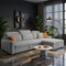 A light gray fabric sectional sofa with a chaise lounge in a modern, warm-toned living room. The sofa is styled with two orange accent pillows, set on a textured cream rug next to a small round white coffee table.