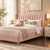 A pink upholstered bed with a tall tufted headboard and matching footboard, styled in a bedroom with patterned wallpaper, white and green bedding, and a pink nightstand. Brand Luxe Maple