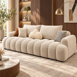 A modern beige tufted sofa with chunky rounded arms and back cushions, styled in a warm contemporary living room with wood paneling, a gold floor lamp, and neutral throw pillows.